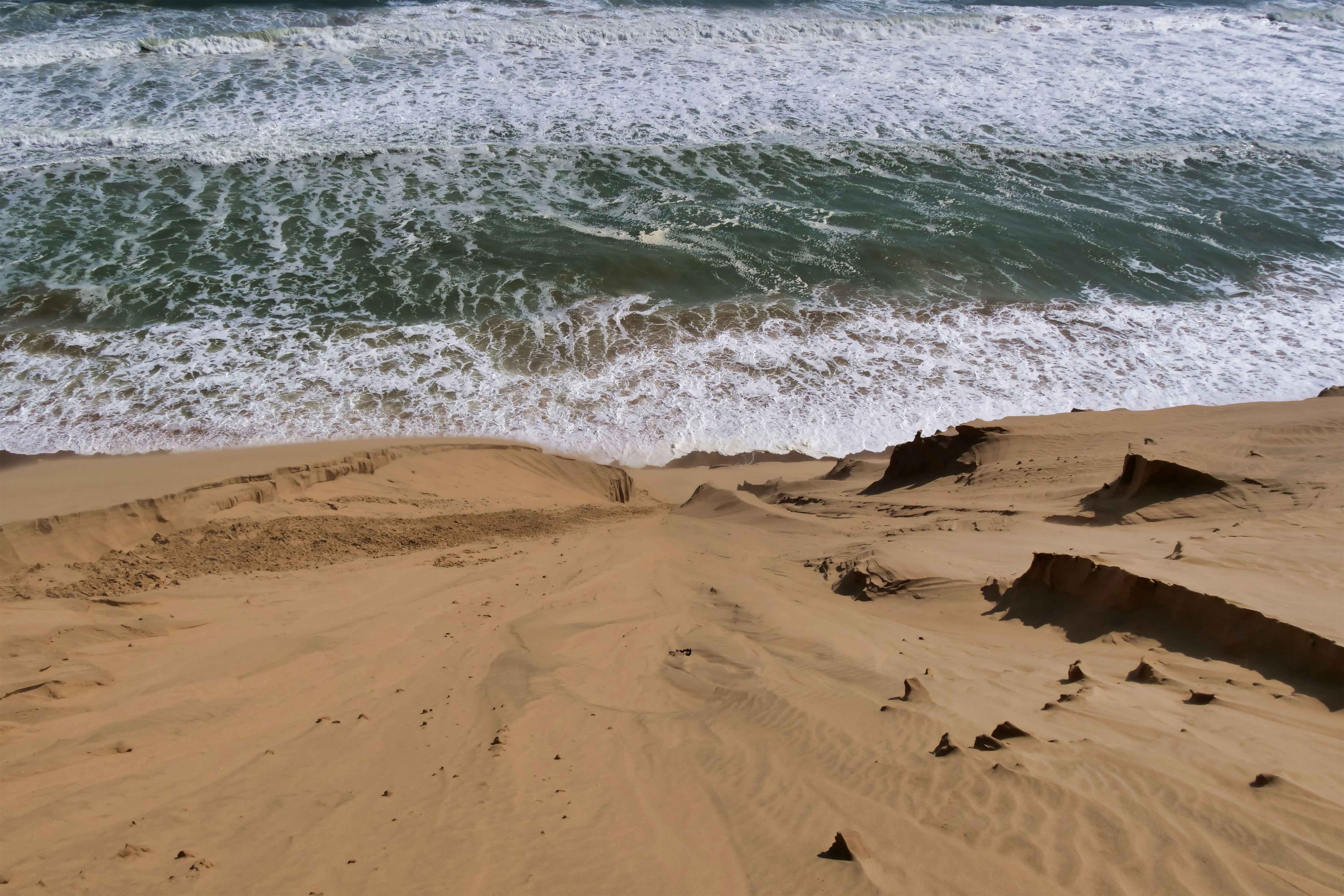 A dramatic landscape of sand dunes cascading into the ocean waves