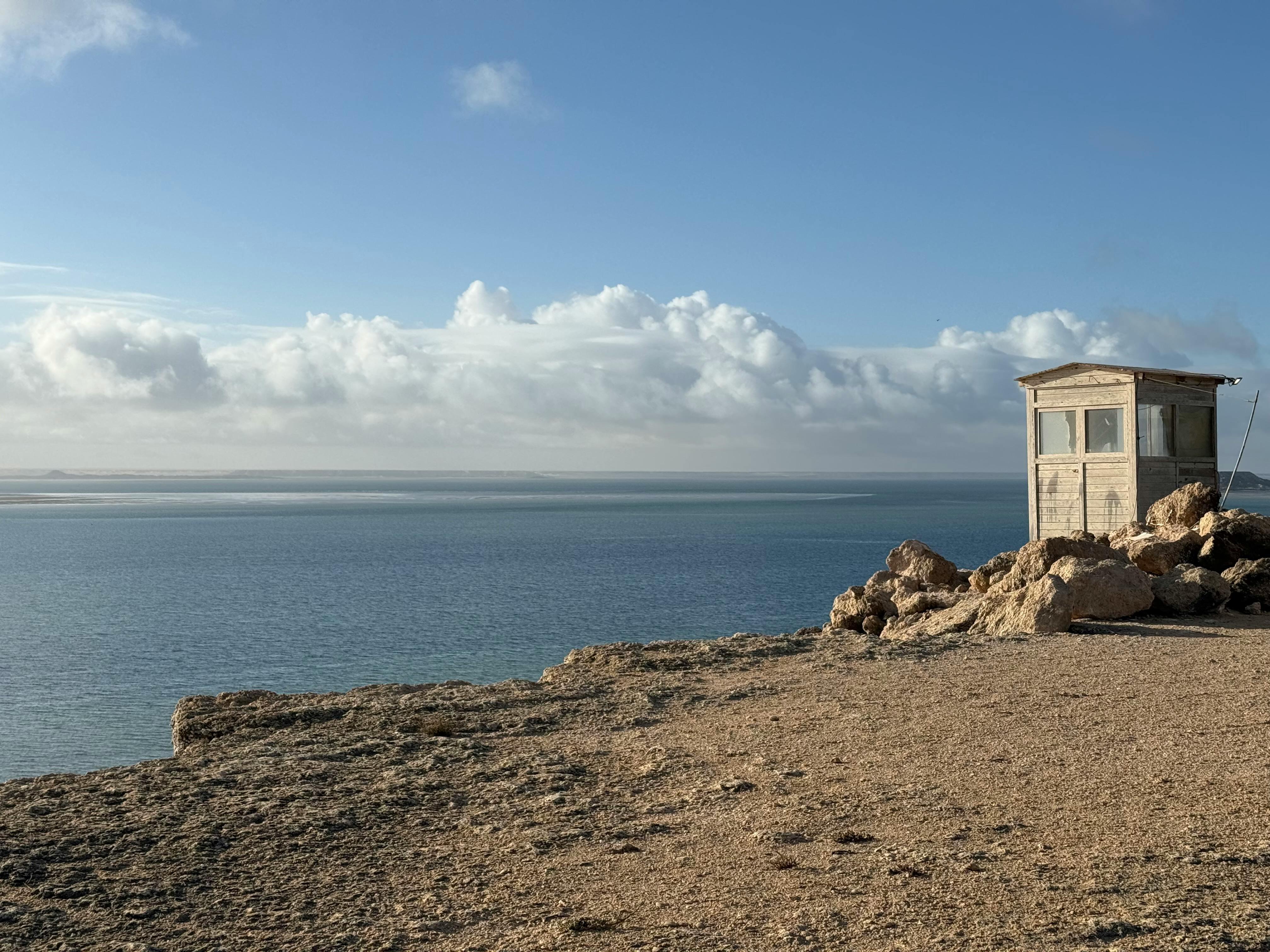 Solitary guard hut on rocky coastline with vast ocean view under bright sky