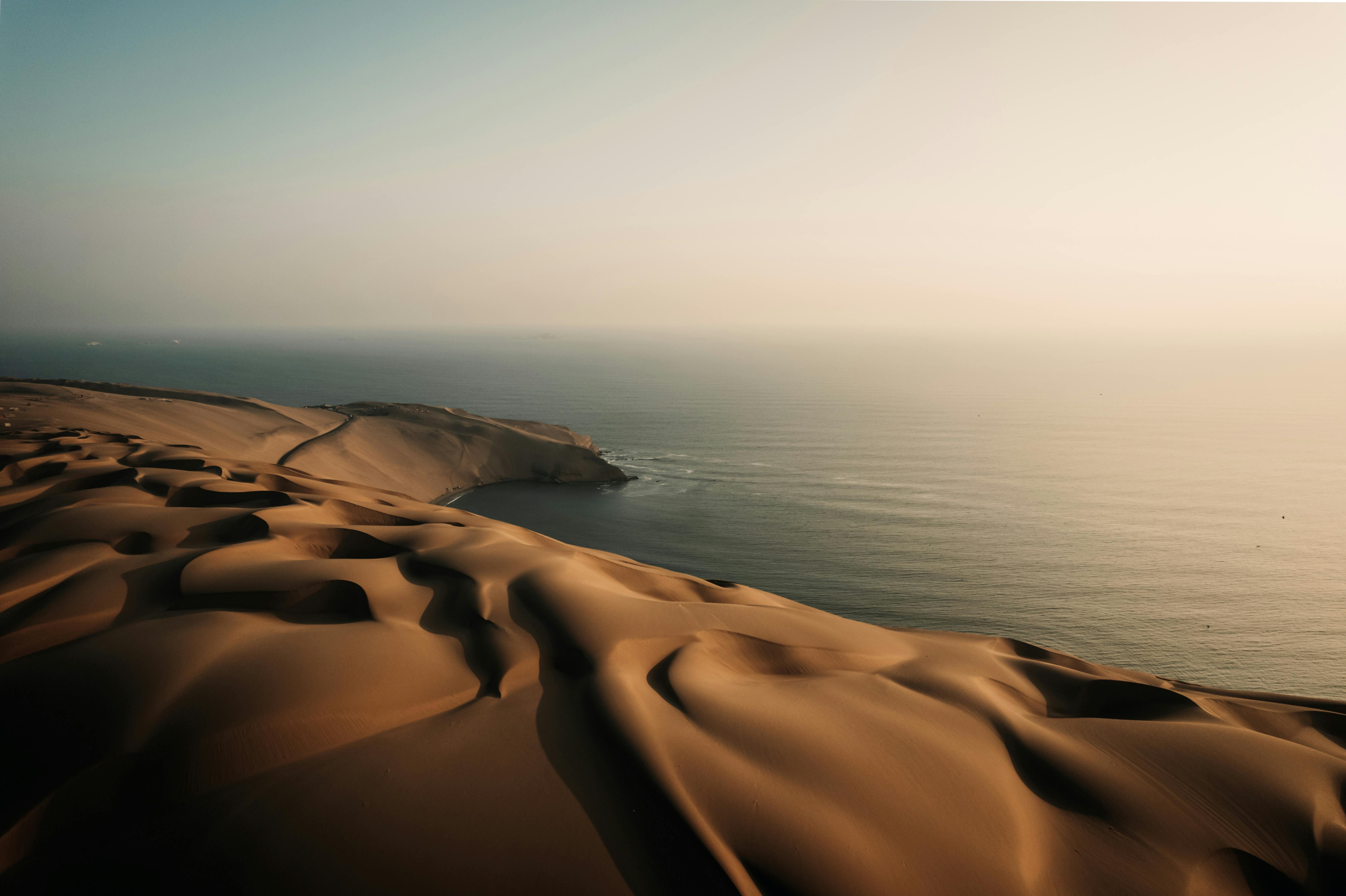 A breathtaking aerial view of undulating desert dunes meeting the vast ocean horizon