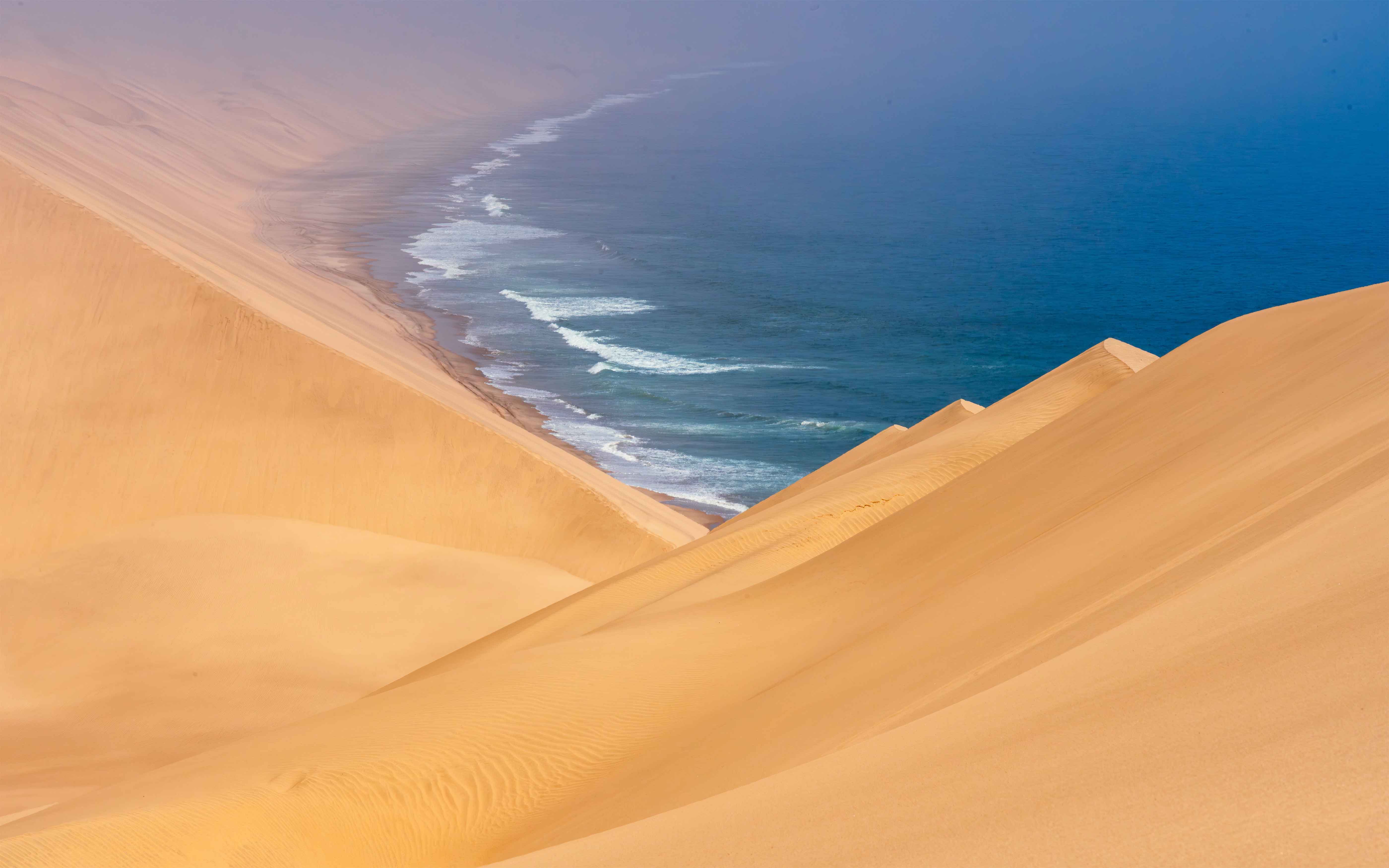 A breathtaking view of vast sand dunes merging with the ocean waves at a remote coastline