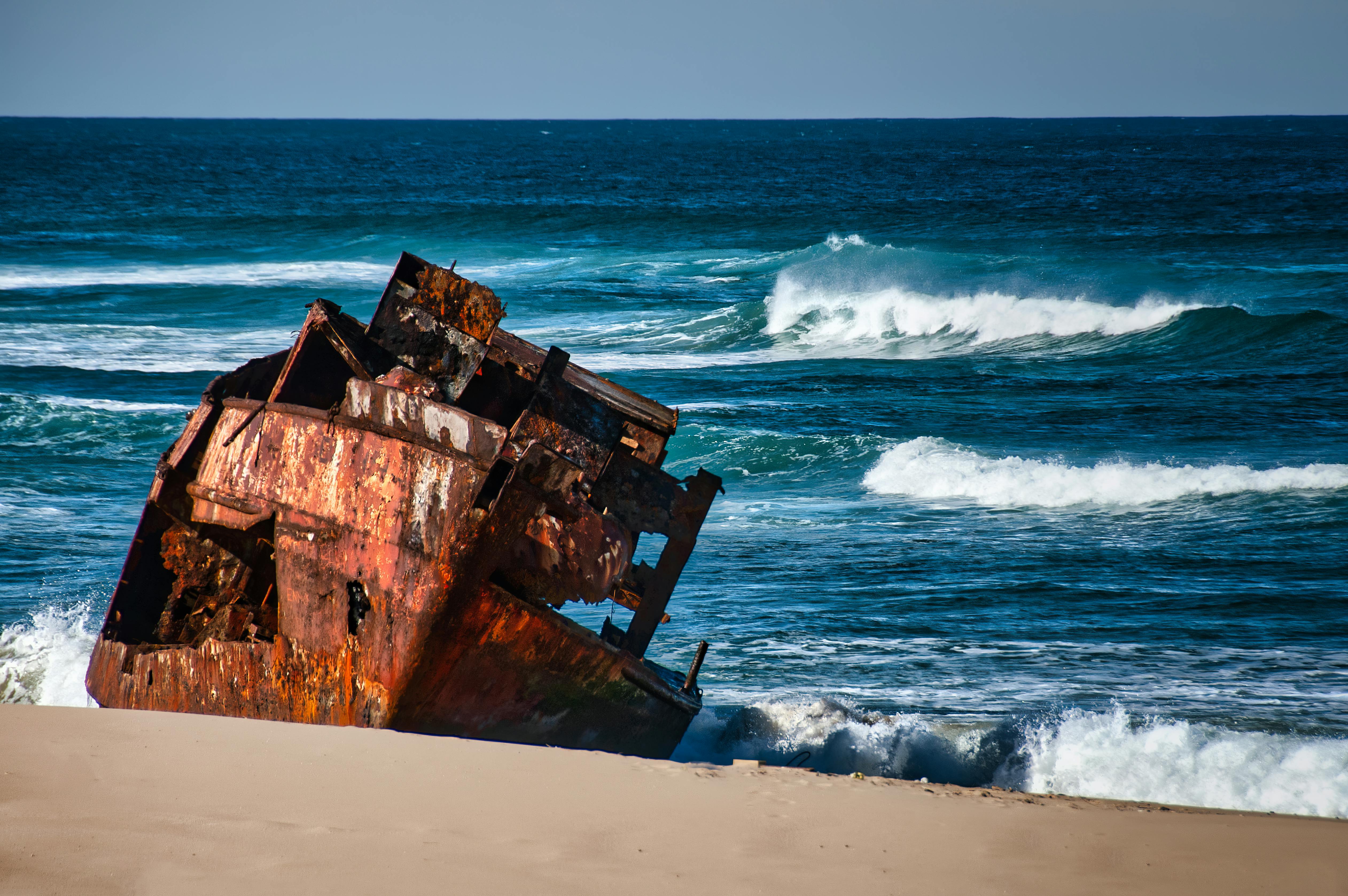A rusted shipwreck on a sandy beach with ocean waves crashing against it