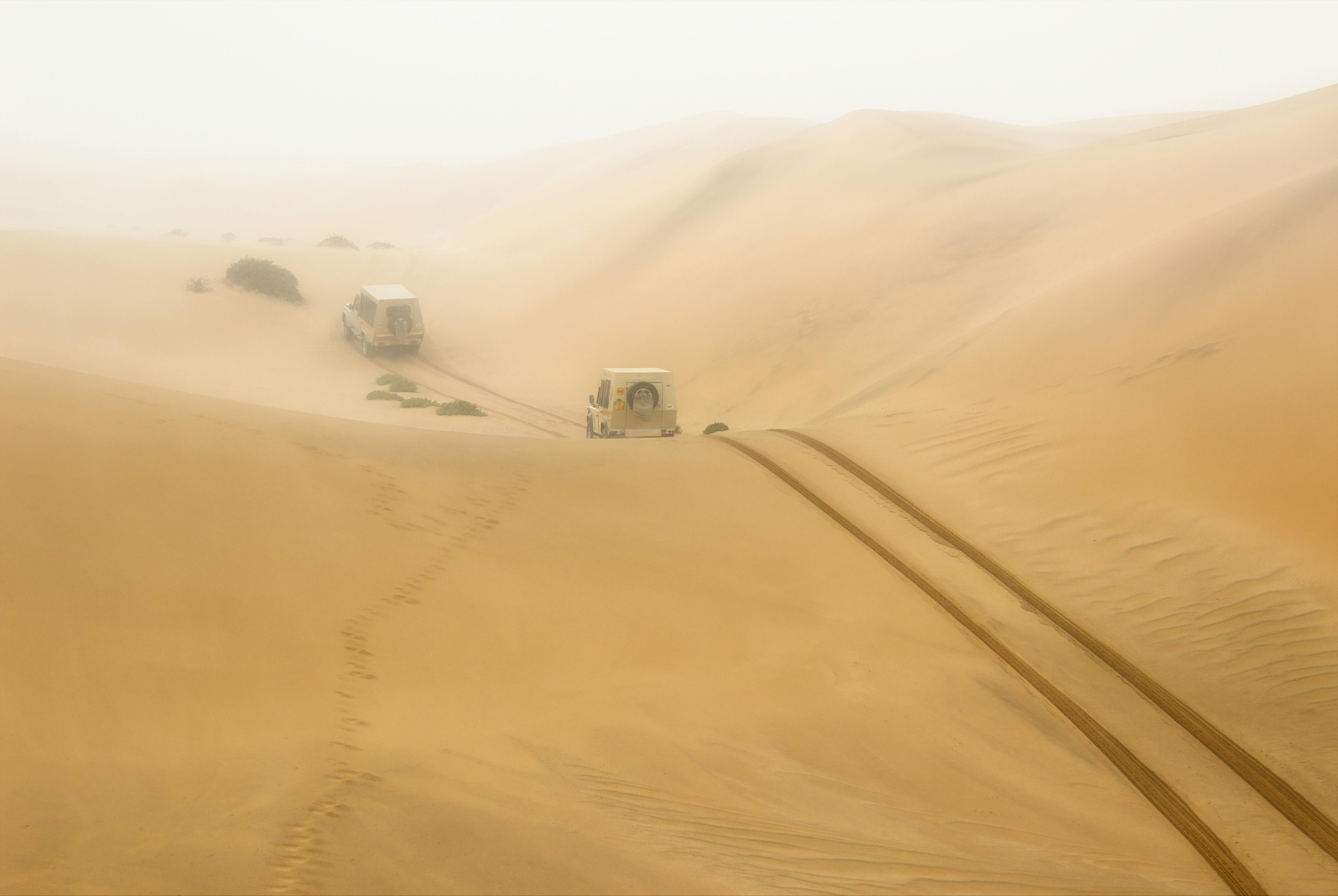 Two vehicles navigate the expansive sand dunes in Namibia Hardap Region